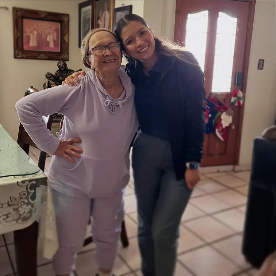 Karla abraza, sonriendo, a una señora mayor en la sala de su casa.