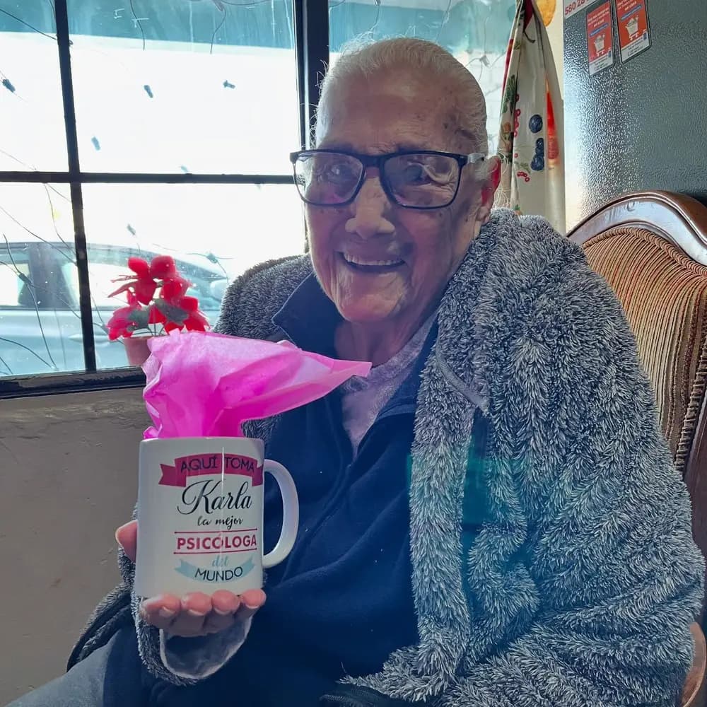 Una paciente sostiene, sonriendo, una taza que dice: Aquí toma Karla, la mejor psicóloga del mundo.